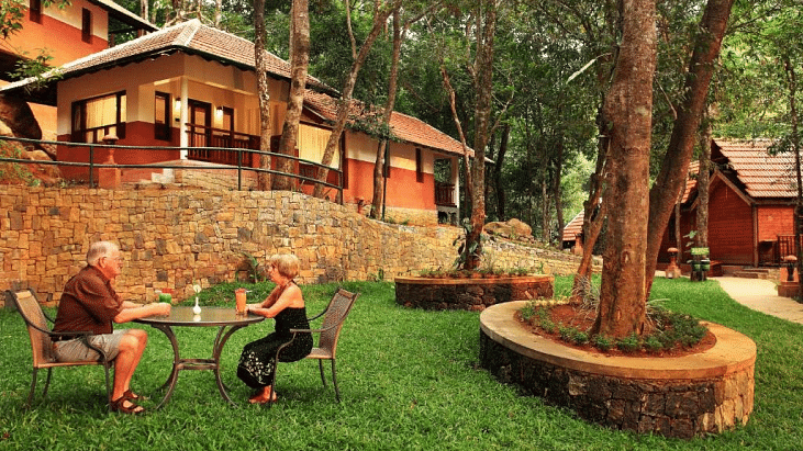 A couple sitting at a table outside the villas, in the greenery | Vythiri Resort, Wayanad